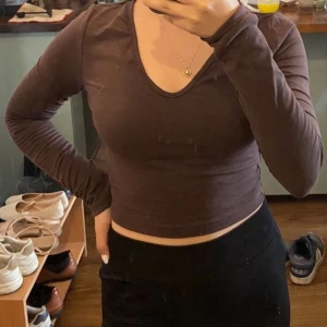 Brun croppad långärmad topp Shein - Säljer en brun croppad långärmad topp från Shein. Toppen har en snygg v-ringning och sitter tight mot kroppen. Perfekt för dig som gillar en enkel men trendig stil. Materialet är mjukt och stretchigt, vilket gör den bekväm att bära.