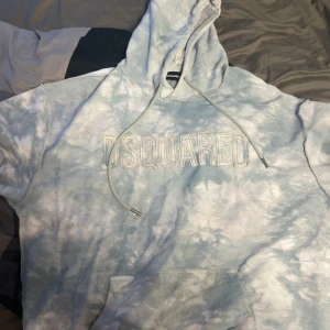 Blå tie-dye hoodie från Dsquared2 - Säljer en soft hoodie från Dsquared2 med ljusblå och vit tie-dye effekt. Stor huva med snörning och stor magficka framtill. Dsquared2-broderi på bröstet ger en clean vibe. Perfekt för chill dagar och streetstyle.