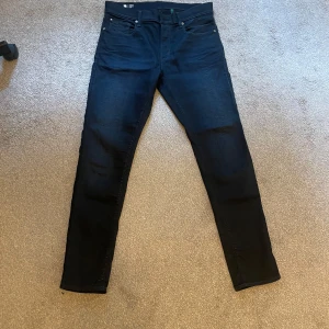 Svarta G-Star RAW 3301 Slim jeans - Säljer ett par svarta G-Star RAW 3301 Slim jeans med klassisk femficksdesign och snygga detaljer på bakfickan. Jeansen har en smal passform och är tillverkade i stretchigt denim för extra komfort. Perfekta för dig som gillar en stilren look.