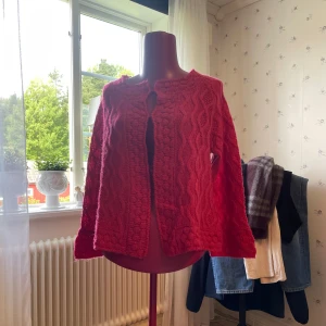 Röd kofta från Jumperfabriken M - Säljer en cerice kofta från Jumperfabriken i storlek M. Koftan har ett snyggt kabelstickat mönster och rund hals. Materialet är en mjuk mix av ull, akryl och alpacka som gör den extra skön och varm. 