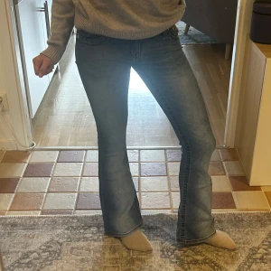Lågmidjade bootcut jeans True Religion - Snygga blå jeans från True Religion med klassisk bootcut-passform och låg midja köpta från Nelly. Jeansen har tydliga sömmar och ikoniska bakfickor med broderad detalj. Materialet är jeans med lätt tvättad look och silverfärgad knapp framtill. Midjemått-37 cm lår mått-21,5 cm innerbenslängd-76,5. Skriv om du undrar något💕
