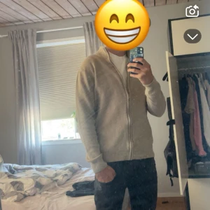 Beige stickad kofta med dragkedja - Säljer en beige stickad kofta från CODE med hel dragkedja framtill och hög krage. Koftan har långärmad passform och är perfekt för lager-på-lager. Enkel och stilren design som funkar till det mesta.