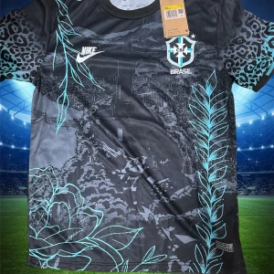 Svart Brasil Nike fotbollströja - Unik svart Brasilien fotbollströja från Nike med coolt tryck av Kristusstatyn och stadssilhuett på framsidan. Ärmarna har leopardmönster i svart och turkos, och hela tröjan är dekorerad med blommor och blad i turkosa linjer. Perfekt för dig som vill sticka ut på planen.