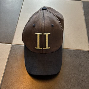 Mörkblå keps från Les Deux - Snygg mörkblå keps från Les Deux med broderad gul logga 'II' framtill och små broderade detaljer i blått, vitt och rött på sidan. Justerbar snapback baktill. Tillverkad i en mix av bomull och polyester för en skön passform.