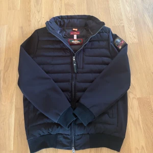 Jacka ifrån Parajumper - Snygg svart jacka från Parajumpers med broderad patch på ärmen. Jackan har quiltad framsida, ribbade muddar och dragkedja framtill. Perfekt för dig som vill ha en stilren och sportig look med premiumkänsla.