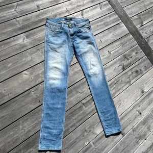 Replay Anbass ljusblå jeans - Säljer ett par Replay Anbass jeans i ljusblå tvätt med snyggt slitna detaljer. Modellen har klassiska fem fickor, raka ben och normal passform. Jeansen är tillverkade i mjukt denimtyg med stretch för extra komfort. Perfekta för en avslappnad och trendig look.