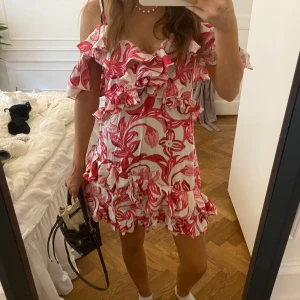 Rosa och vit blommig volangklänning - Supersöt kort klänning med rosa och vitt blommönster, volanger och offshoulder-ärmar. Perfekt för sommardagar och har en luftig, romantisk vibe. Klänningen har flera lager volanger och en feminin passform. En långklänning från HM som jag sytt om till kort! Så är alldeles unik!!🩷🩷💛💛💛