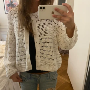 Vit stickad kofta med hålmönster - Superfin vit stickad kofta med hålmönster och raka ärmar. Koftan har en lite boxig passform och knappar framtill. Perfekt att slänga över ett linne eller t-shirt för en chill och trendig look.