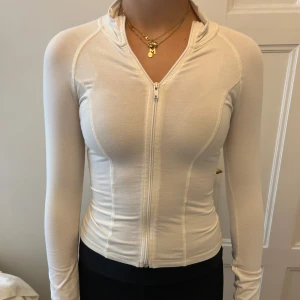 Vit tight hoodie - Supersnygg vit hoodie från Gina Tricot i tight passform. Tröjan har hel dragkedja framtill, lång ärm och hög krage. Perfekt för dig som gillar en clean och sportig look. Materialet är mjukt och stretchigt, vilket gör den riktigt bekväm.