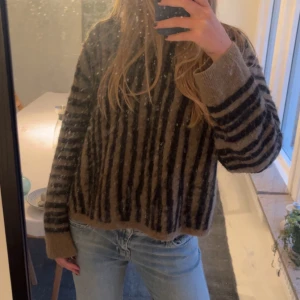 Randig stickad tröja & Other Stories - Supermysig stickad tröja från & Other Stories med bruna och svarta ränder. Oversized passform, rund hals och långa ärmar. Perfekt för lager-på-lager och chill höstkvällar. Materialet är mjukt och fluffigt, vilket gör den extra skön att bära.