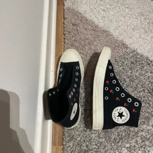 Svarta Converse med broderade rosor - säljer utan skosnören! använt bara fåtal gånger. Snygga svarta Converse high-tops med vita sulor och broderade små röda rosor på sidorna. Klassisk rund tå och platt sula. Skorna är i textil med Converse-logga på sidan och passar perfekt för dig som vill ha en unik twist på dina sneakers.
