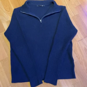 Marinblå stickad tröja med half zip - Säljer en marinblå stickad tröja i storlek S. Tröjan har en ribbad struktur, lång ärm och en snygg half zip-dragkedja vid kragen. Perfekt för dig som gillar stilrena och bekväma plagg.