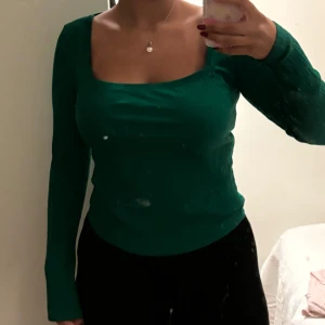 Grön ribbad långärmad topp - Snygg grön långärmad topp med fyrkantig urringning och ribbad struktur. Figurnära passform som framhäver siluetten och ger en modern vibe. Perfekt att styla med jeans eller kjol för en trendig look. Väl använd men i bra skick fortfarande. 