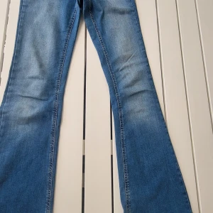 Blå bootcut jeans med dragkedja - Snygga blå bootcut jeans med klassisk femficksdesign och dragkedja fram. Jeansen har en lätt tvättad look och sitter tajt upptill med utsvängda ben. Perfekta för dig som gillar retrovibbar och vill ha en bekväm passform.
