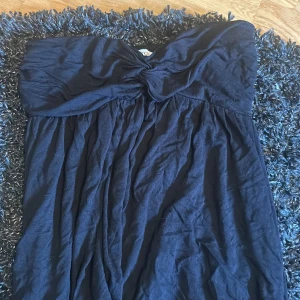 Marinblå axelbandslös kortklänning - Snygg marinblå kortklänning med axelbandslös design och twistad detalj vid bysten. Klänningen har ett mjukt, fallande tyg som ger en avslappnad och elegant look. Perfekt för dig som gillar stilrena och enkla plagg med en twist.