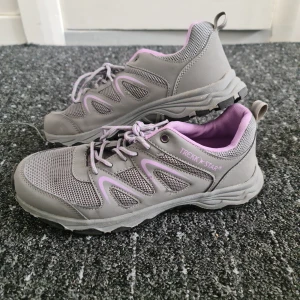 Grå och lila sneakers från Trekk Star - Snygga grå sneakers med lila detaljer och meshpartier från Trekk Star. Skorna har snörning, robust sula och bekväm passform. Perfekta för dig som gillar en sportig stil och vill ha något som sticker ut med coola färgkombinationer.