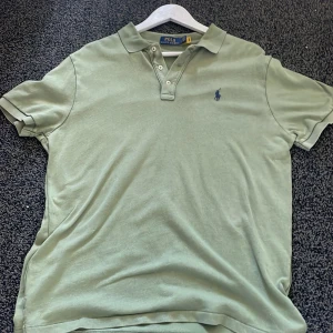 Grön pikétröja från Polo Ralph Lauren - Snygg ljusgrön pikétröja från Polo Ralph Lauren med klassisk krage, tre knappar och broderad logga på bröstet. Tillverkad i mjuk bomull och har korta ärmar. Perfekt för en chill och stilren look.