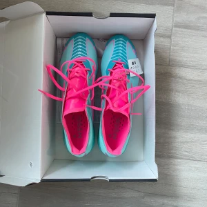 Adidas Messi fotbollsskor turkos/rosa - Snygga Adidas Messi fotbollsskor i turkos och neonrosa med coola detaljer och snörning. Skorna har en smal, sportig form och är tillverkade i syntetmaterial för bästa grepp och känsla på planen. Kommer med matchande påse med Messi-tryck. Helt oanvända pågrund av att jag köpt fel storlek.