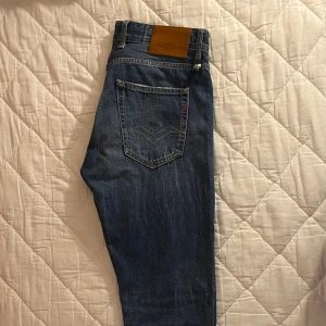 Replay Grover blå jeans straight fit - Snygga Replay Grover jeans i klassisk blå tvätt med straight fit. Jeansen har slitna detaljer, fem fickor och tydliga kontrastsömmar. Märkespatch i brunt läder baktill och Replay-logga vid fickan i rött. Tveka inte på att ställa frågor🫡 