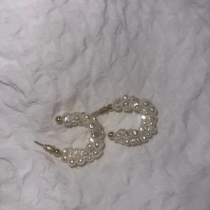 Hoop-örhängen med pärlor - Säljer ett par snygga hoop-örhängen dekorerade med vita pärlor i olika storlekar. Örhängena har en rund form och detaljer i guld vid fästet. Perfekt för dig som vill ha en elegant och trendig accessoar.