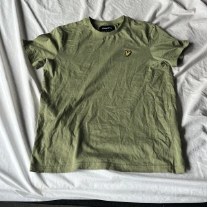 Grön t-shirt från Lyle & Scott - Snygg grön t-shirt från Lyle & Scott med klassisk rund hals och korta ärmar. På bröstet sitter den ikoniska broderade gula örnen. T-shirten är gjord i mjuk bomull och har en clean, enkel look som funkar till jeans eller shorts.