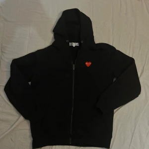 Svart zip hoodie Comme des Garçons Play XL - OBS!!!! Tröjan är i vanlig storlek M.                    Svart hoodie från Comme des Garçons Play i storlek XL i barnstorlek/ M i vanlig storlek, vuxenstrolek! Tröjan är i nyskick och använd runt 5 gånger. Jag är 184 och passar mig bra men hade lätt passat från 182 - 186
