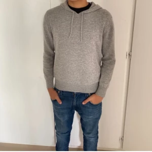 Grå kashmir hoodie från Sayless - Mjuk och stilren grå hoodie från Sayless i lyxig kashmir. Tröjan har huva med snörning, lång ärm och ribbade muddar. Perfekt för dig som gillar en clean look med premiumkänsla. Passar dig som vill ha en hoodie med lite mer exklusiv vibe.