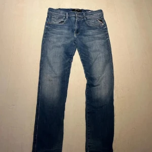 Replay Anbass jeans blå, stl 31 - Säljer ett par snygga Replay Anbass jeans i klassisk blå tvätt. Modellen har raka ben, fem fickor och coola detaljer på bakfickan. Jeansen är i bomull och har en normal passform som funkar till det mesta. Perfekta för dig som gillar stilrena och tidlösa jeans.