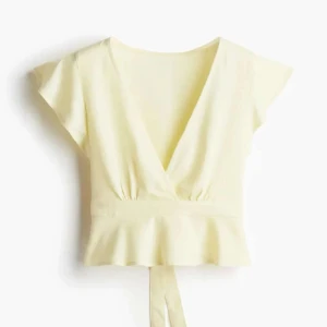 Säljer en Ljusgul omlottopp med volang då den ej är till användning längre  - Superfin ljusgul omlottopp med v-ringning och volang nertill. Toppen har korta ärmar och knytband i midjan för en snygg passform. Perfekt för dig som gillar en feminin och fräsch stil.