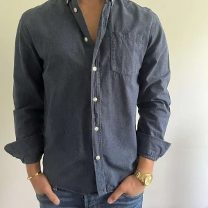 Mörkblå skjorta - Snygg mörkblå skjorta med klassisk krage och vita knappar hela vägen framtill. Skjortan har en bröstficka på vänster sida och långa ärmar med knapp vid manschetten. Passformen är normal och passar dig som vanligtvis har storlek S-M. Materialet känns som mjuk bomull. Pris kan diskuteras