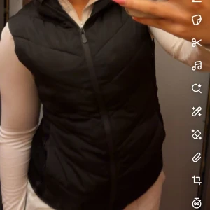 Zaraväst  - Snygg svart zaraväst med dragkedja framtill och lätt quiltad design. Perfekt att slänga över en hoodie eller långärmad tröja för extra värme. Västen har en klassisk passform och är enkel att matcha med olika outfits. 