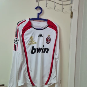 AC Milan långärmad Kaka 22 tröja - Säljer en officiell AC Milan långärmad fotbollströja från Adidas med Kaka och nummer 22 på ryggen. Tröjan är vit med röda och svarta detaljer, Champions League-märke på ärmen och Bwin som sponsor på bröstet. Materialet är lätt och andas, perfekt för match eller samling.