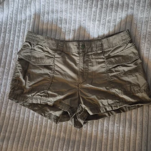 Beiga cargoshorts från H&M Divided - Snygga beiga cargoshorts från H&M Divided i 100% bomull. De har två stora fickor framtill, bälteshällor och en relaxed passform. Perfekta för varma dagar när du vill ha en chill och praktisk stil.