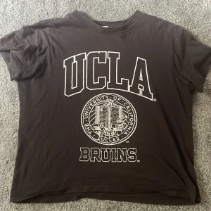 Svart UCLA t-shirt från H&M XS - Svart t-shirt från H&M i samarbete med UCLA, storlek XS. Stor vit UCLA-logga och universitetsmärke framtill. Klassisk passform med rund hals och korta ärmar. Perfekt för dig som gillar college-vibe och streetstyle. Har en liten färgfläck på axeln men går säkert bort med nått medel. Är lite solblekt.