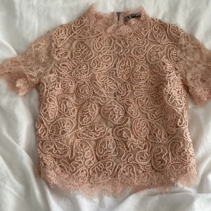 Beige/ljus rosa spetsblus från Zara Trafaluc - Supersöt beige spetsblus från Zara Trafaluc med korta ärmar och hög hals. Blusen har vackra spetsdetaljer, broderat mönster och dragkedja i ryggen!!💗