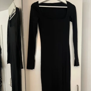 Svart långärmad klänning - En stilren svart långklänning med lång ärm och fyrkantig ringning. Klänningen har en tight passform och är perfekt för dig som gillar minimalistisk stil. Materialet känns mjukt och stretchigt, vilket gör den bekväm att bära hela dagen.
