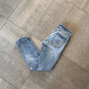 Taylor Tweed Jeans - Ljusblå Taylor Tweed jeans med snygga slitningar och lätt tvättad look. Klassisk femficksmodell med rakt snitt och röda detaljer. Stolek:31