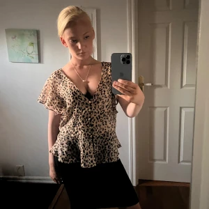 Leopardmönstrad blus med volang - Säljer en luftig blus med leopardmönster i beige och svart. Blusen har v-ringning, knappar framtill och korta, volangiga ärmar. Materialet är tunt och känns som polyester, perfekt för en trendig look.