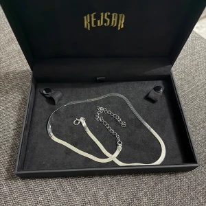 Silvrigt halsband från Kejsar 53cm - Snyggt och stilrent halsband från Kejsar i silverfärg. Kedjan är platt och glänsande med justerbar längd, totalt 53 cm. Perfekt för att ge din outfit en clean och modern touch. Levereras i original ask med Kejsar-logga. Helt nya oanvända Vid retur står köparen för Frakten/Returen. Jag ansvarar inte för postens slarv.