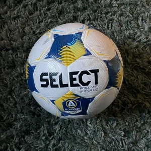 Select Allsvenskan fotboll, storlek 5 - Officiell Allsvenskan fotboll från Select, modell Brillant Super UZ. Bollen är vit med blå och gula detaljer samt Allsvenskan-logga. Tillverkad i slitstarkt syntetmaterial och har en klassisk rund form med texturerad yta för bättre grepp. Match använd i allsvenskan i matchen mellan IF ELFSBORG och BK HALMSTAD fick den av en kompis som nämligen spelar i Elfsborg ny pris på bollen är 2000kr