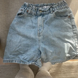 Ljusblå jeansshorts från Zara - Säljer ett par ljusblå jeansshorts från Zara med högmidjad passform och elastisk midja. Shortsen har klassiska fickor fram och bak, samt bälteshällor. Perfekta för sommarens chill dagar och har en loose fit som ger skön vibe.