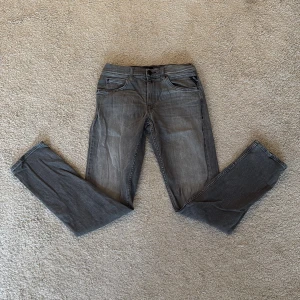 Replay grå jeans slim fit - Snygga grå jeans från Replay med klassisk femficksdesign och diskret Replay-logga vid fickan. Jeansen har en rak passform och är tillverkade i mjukt jeanstyg som sitter skönt. Perfekt för dig som gillar stilrena och tidlösa jeans.
