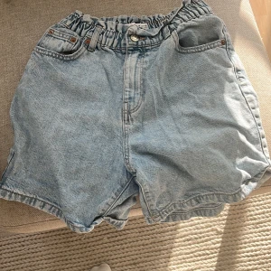 Ljusblå jeansshorts från Zara - Säljer ett par ljusblå jeansshorts från Zara med loose passform och högmidjad, rynkad midja med knapp och dragkedja. Shortsen har klassiska fickor fram och bak, samt bälteshällor. Perfekta för chill dagar under sommaren.