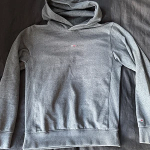 Grå hoodie från Tommy Jeans XS - Snygg grå hoodie från Tommy Jeans i storlek XS. Tröjan har huva, långa ärmar och diskret logga på bröstet samt liten flagga på ärmen. Mjuk bomullsmix som är perfekt för chill dagar. Klassisk passform och stilren look.
