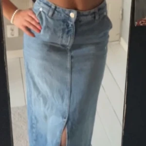 Lång jeanskjol med slits  - Säljer en snygg lång jeanskjol från NA-KD i klassisk blå denim. Kjolen har en rak passform, hög midja och en slits framtill och baktill🦋💙