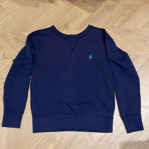 Mörkblå tröja från Polo Ralph Lauren - Säljer en stilren mörkblå tröja från Polo Ralph Lauren med det klassiska logotypen broderad i ljusblått på bröstet. Fint skick!
