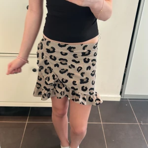 Leopardmönstrad kjol med volang - Trendig kortkjol med leopardmönster i beige och svart. Kjolen har en volangdetalj längs nederkanten som ger en lekfull touch. Perfekt för att sätta en djärv stil på din outfit.