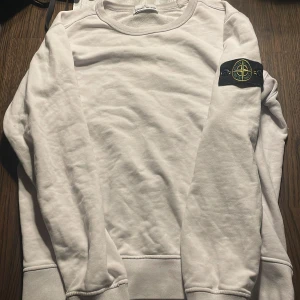 Vit sweatshirt från Stone Island - Säljer en stilren vit sweatshirt från Stone Island med deras ikoniska märke på ärmen. Tröjan har långa ärmar och ribbade muddar vid ärmslut och nederkant. Perfekt för en casual look. Nackdelar är att den har lite fläckar på armen som tyvär går inte bort.