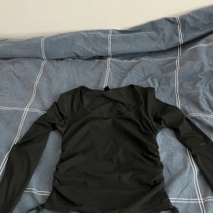 Svart ribbad topp med snörning - Snygg svart ribbad topp med långa ärmar och snörning i sidorna. Perfekt för en stilren look. Passar bra till både jeans och kjol.