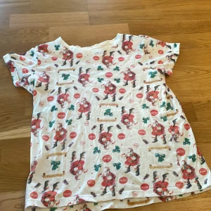 Vit julig t-shirt med tomtemönster - Säljer en vit t-shirt med ett festligt tomtemönster. Perfekt för julfirandet! T-shirten har korta ärmar och är täckt med glada tomtar och julmotiv. En rolig och lekfull design för den som älskar julen 🎅